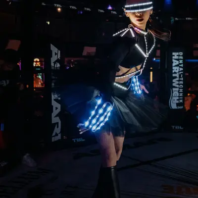 TBL Events performer in a futuristic illuminated outfit inside an MMA fight cage during a live combat sports event.