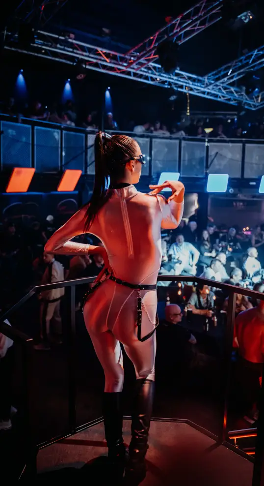 Female performer dancing on stage at a lively nightclub event with colorful stage lighting and a large crowd.