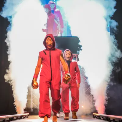 Two performers in red hooded outfits walking onto a stage through dramatic clouds of smoke at a live combat sports event.